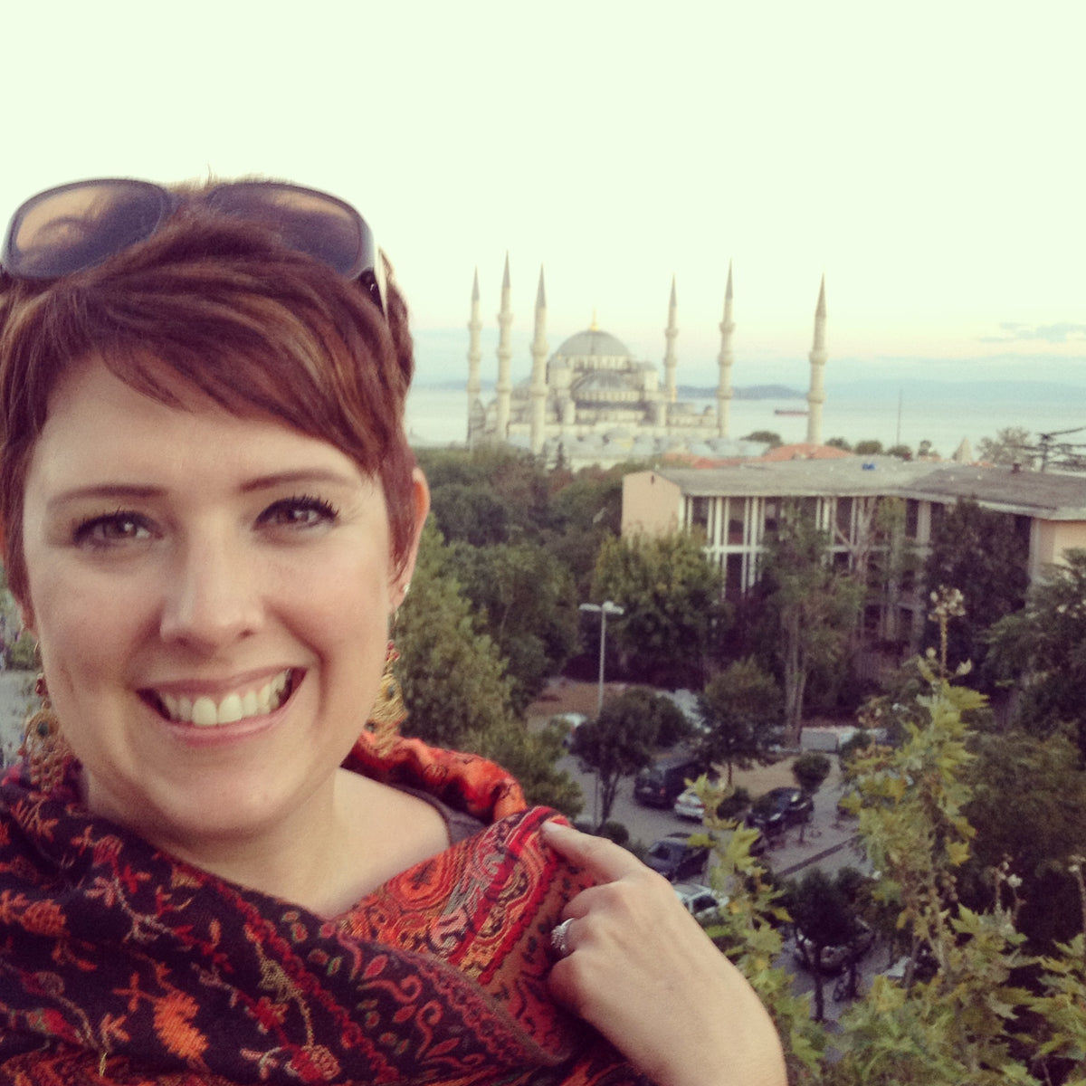 Selfie of business owner wearing a red shawl. She has short red hair. Located in Istanbul in front of the Blue Mosque