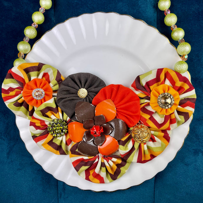 60's Multi-Colored Flower Bomb Necklace with Brown & Orange Vintage Flower Brooch, Green Beaded Chain on a white plate