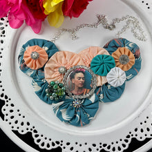 Load image into Gallery viewer, 1940&#39;s Teal Fabric with Peach &amp; White yo-yos &amp; Teal Frida Pendant Necklace on a white plate with colorful flowers in the top left corner
