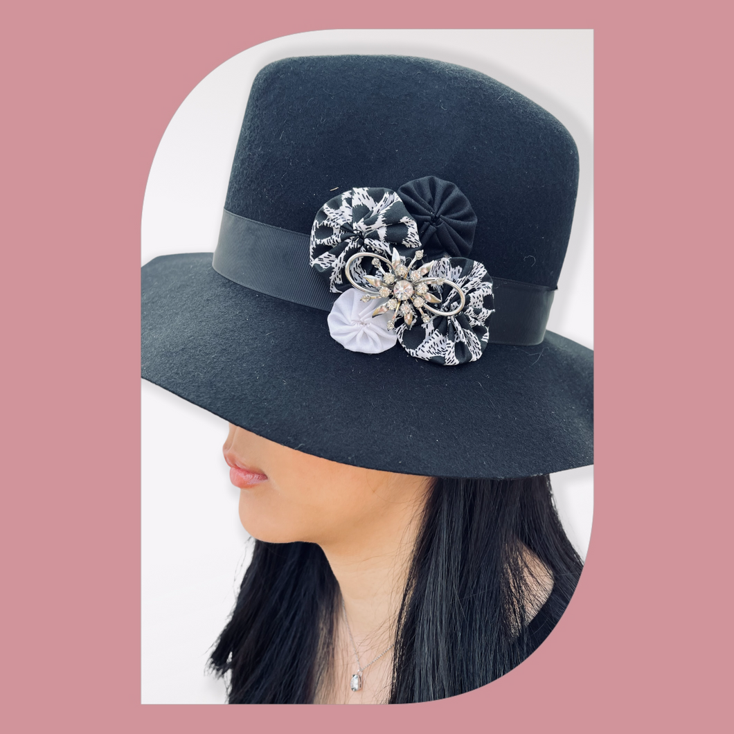 Black Floppy Hat with Leopard Fabric Flowers & Vintage Pin on a model facing left. Pink background