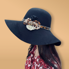 Load image into Gallery viewer, Black Floppy Hat with leopard and black Yo-yos and an orange pin. Side profile of a model with long black hair
