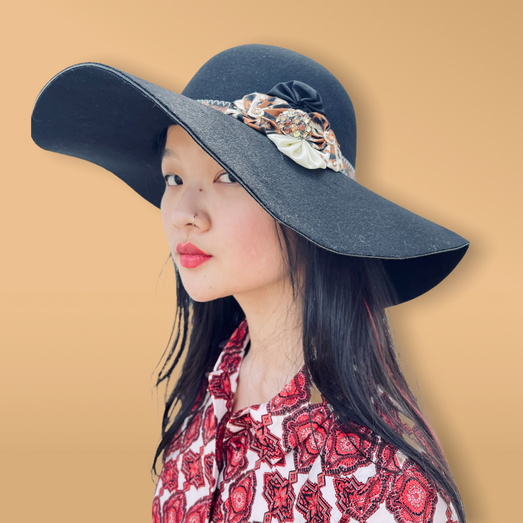 Black Floppy Hat with leopard and black Yo-yos and an orange pin. Side profile of a model with long black hair